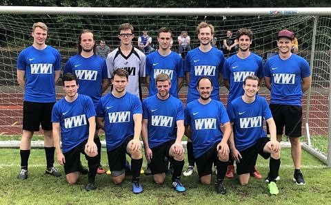 Eine Fußballmannschaft in blauen Trikots mit dr Aufschrift WW1, die sieben Spieler in der hinteren Reihe stehen, die in der vorderen Reihe knien auf einem Knie.